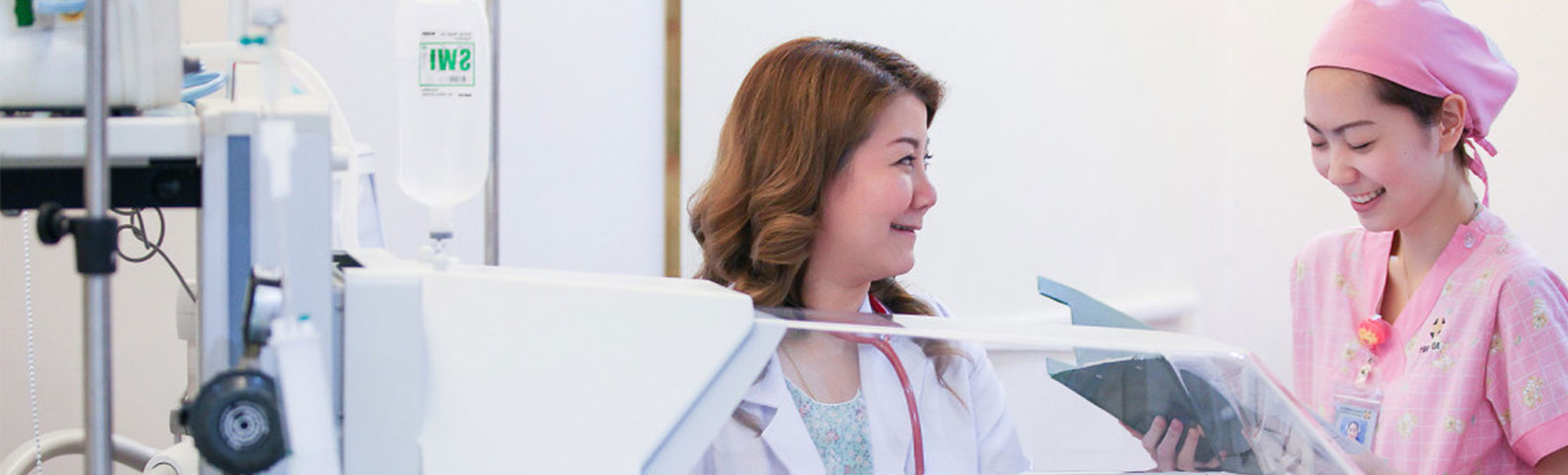 Eine Krankenschwester und eine Ärztin lächeln gemeinsam in einer Babystation im Krankenhaus.